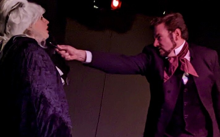 A dramatic two-hander scene on stage under coloured light