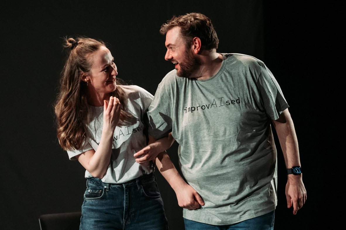 Emily Matthews and Tom Gilder smiling during a FinFringe performance of ImprovAIsed